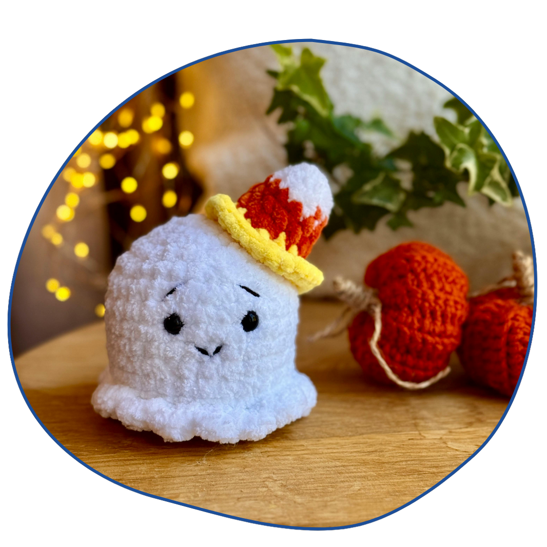 Crocheted ghost toy with candy corn hat on a wooden surface with blurred lights and plants in the background