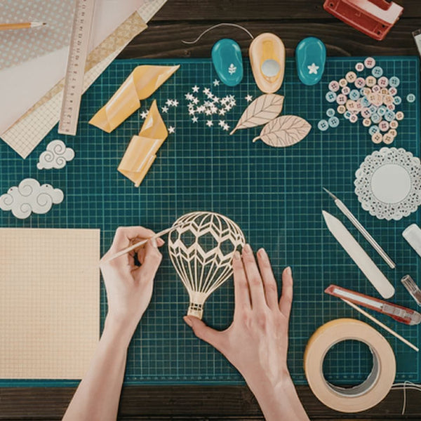 Hands working on a craft project with cut-out shapes on a green cutting mat.