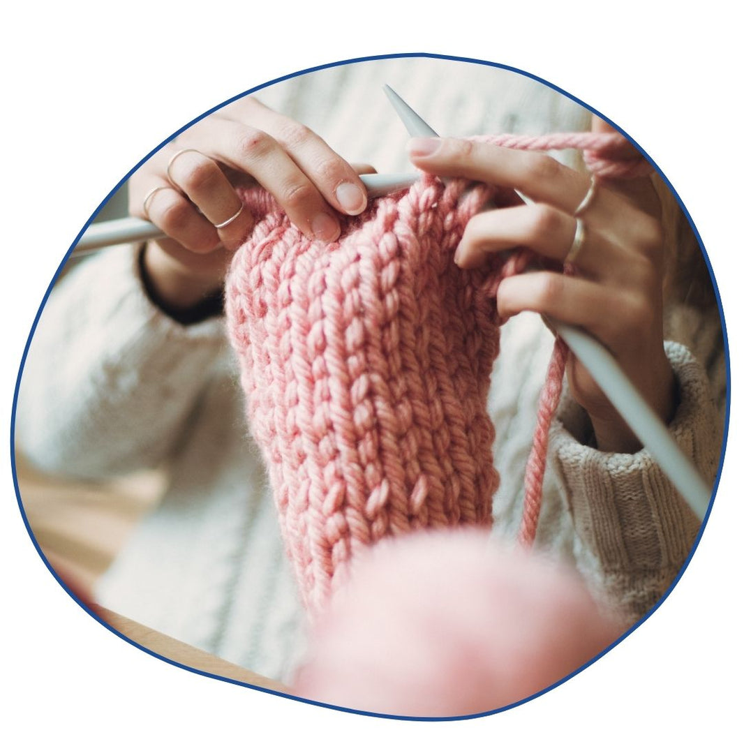 Close-up of hands knitting a pink sweater with a blurred background