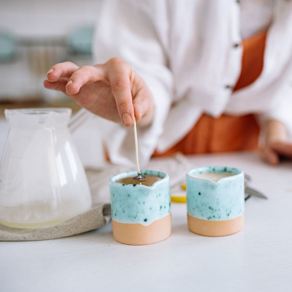 Person pouring liquid into two small ceramic cups with a speckled design.