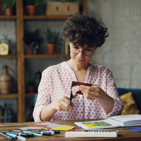 Woman with glasses holding a card in a room with a bookshelf and plants.